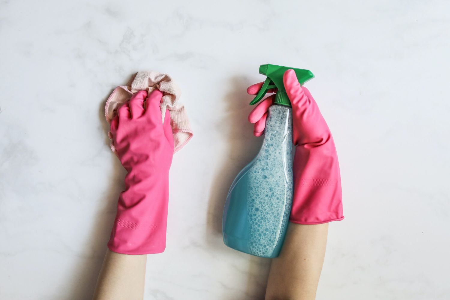 A person wearing pink gloves and cleaning a surface with soup in the spray bottle.